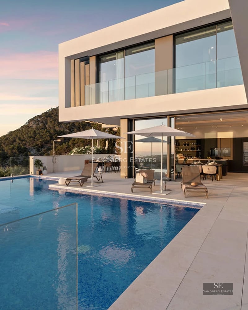 Wide view of a modern villa with an infinity pool, large windows, and lush garden. Minimalist architecture.