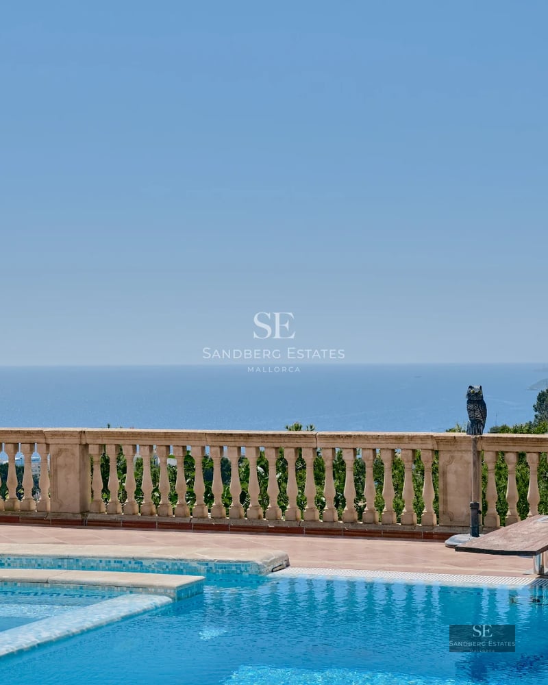 Panoramic view of an infinity pool with sun loungers, surrounded by greenery and modern, minimalist architecture.