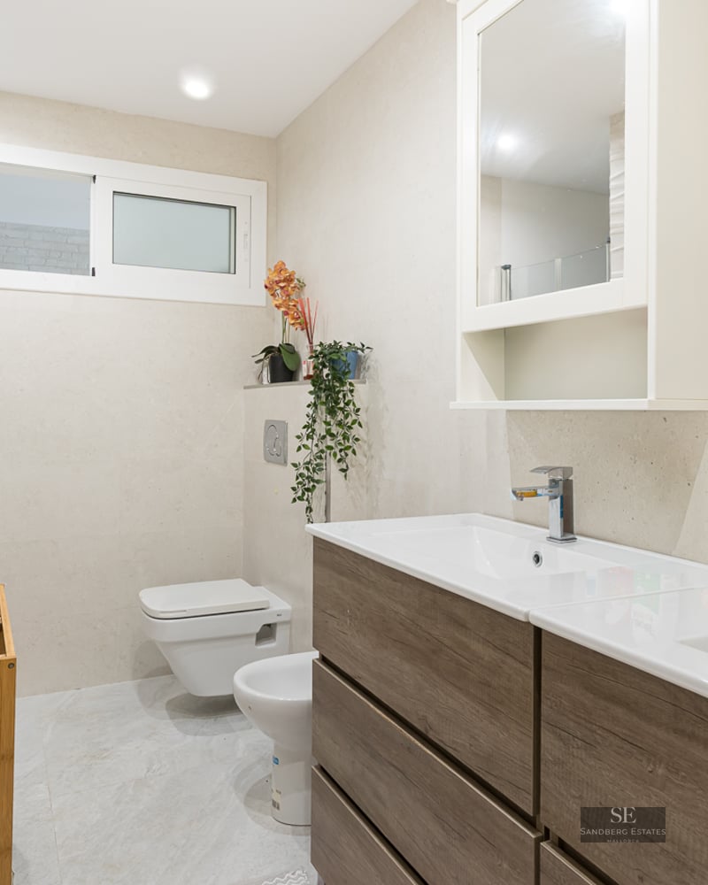 Modern bathroom with wood-finish double vanity, textured wall tiles, wall-hung toilet, and bidet.