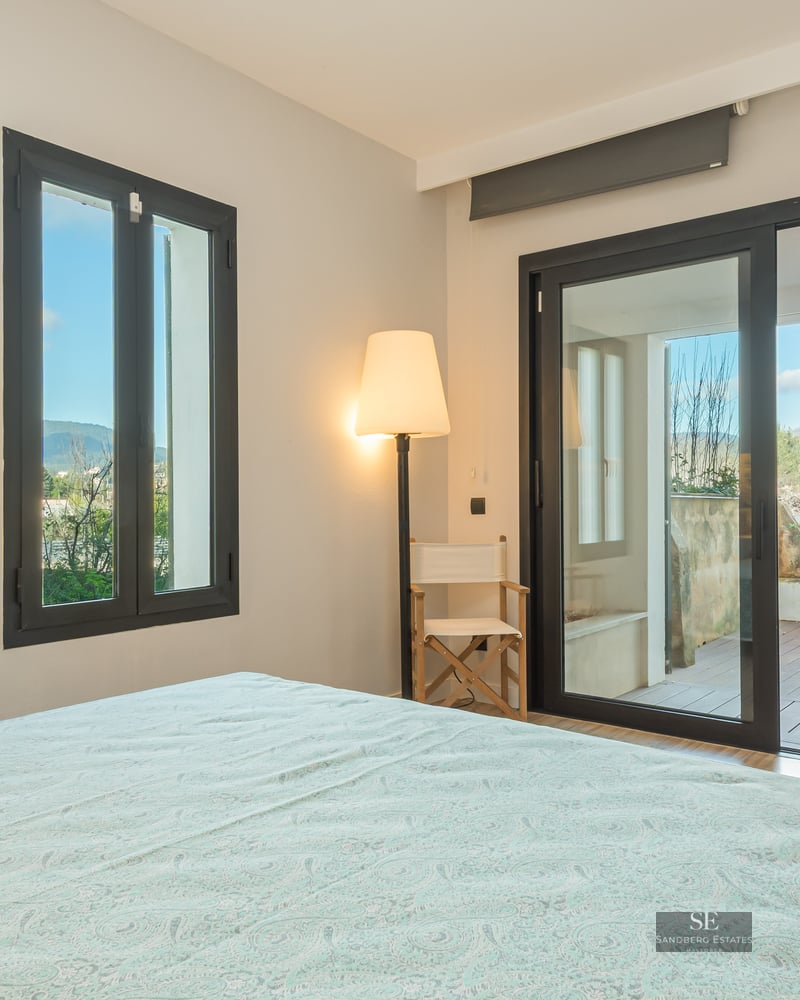 Bright bedroom with sliding glass doors opening to a wood-decked terrace with mountain views.