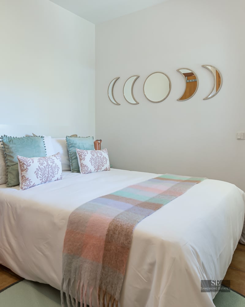Bedroom with a white bed, terracotta tile floors, and moon phase mirrors above the headboard.