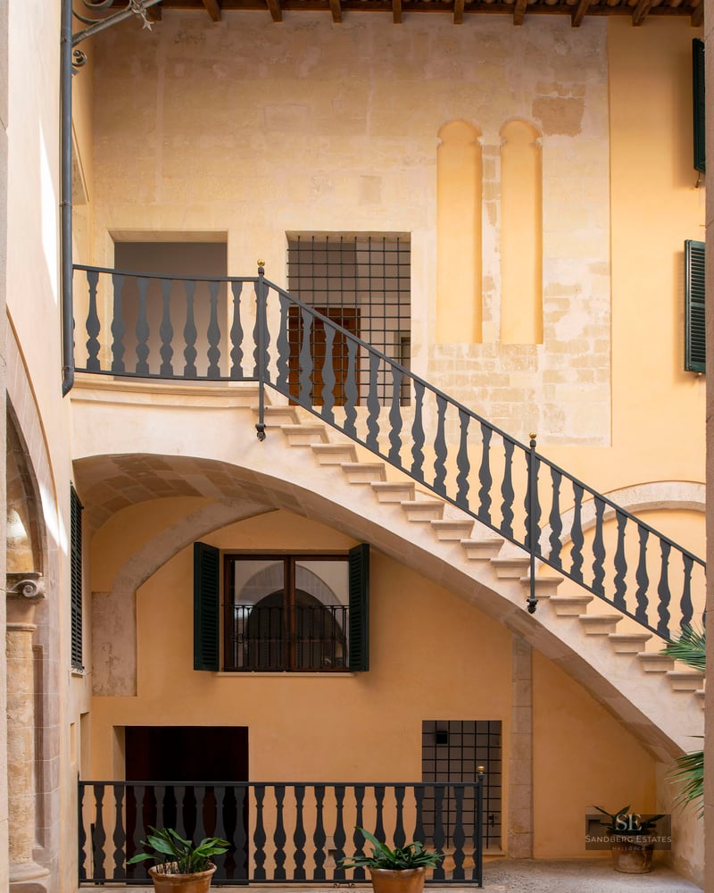 View of an inner courtyard with a stone staircase, black wrought iron railings, and warm ochre stone walls.