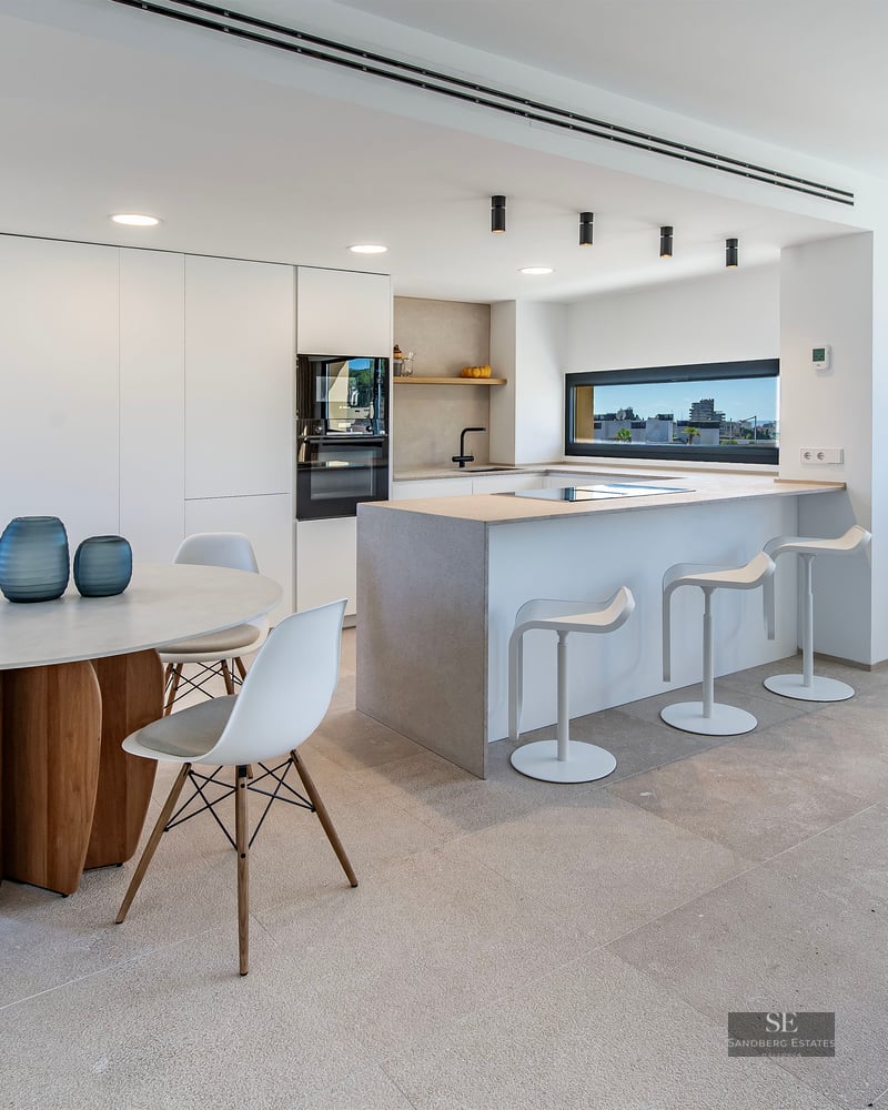 Modern kitchen with stone island, breakfast bar, and round dining table near a window with a city view.