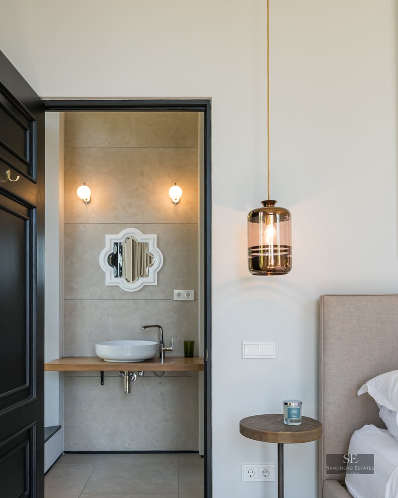 Luxury bedroom with black door leading to a modern ensuite bathroom, featuring a large painting and pendant light.
