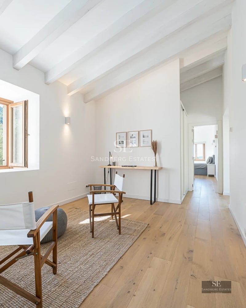 Spacious living room with large windows, light wood floor, grey modular sofa, and view of lush garden. Modern and elegant design.
