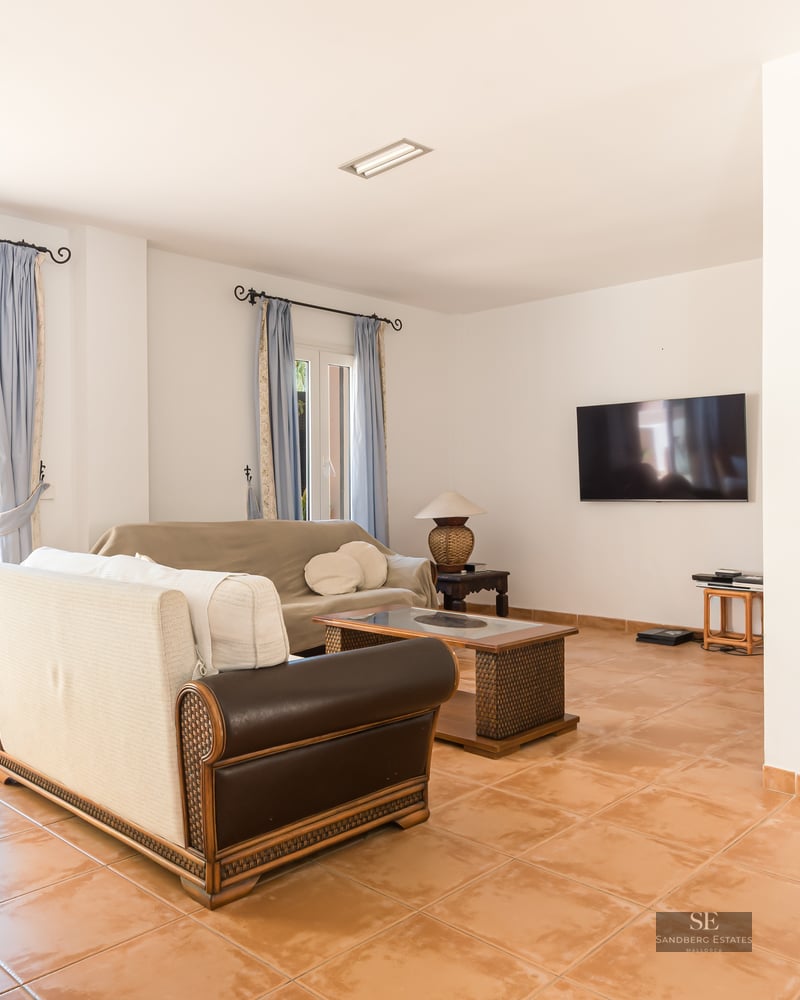 Spacious living room with terracotta floors, sofas, and a large sliding glass door opening to a flowery terrace.