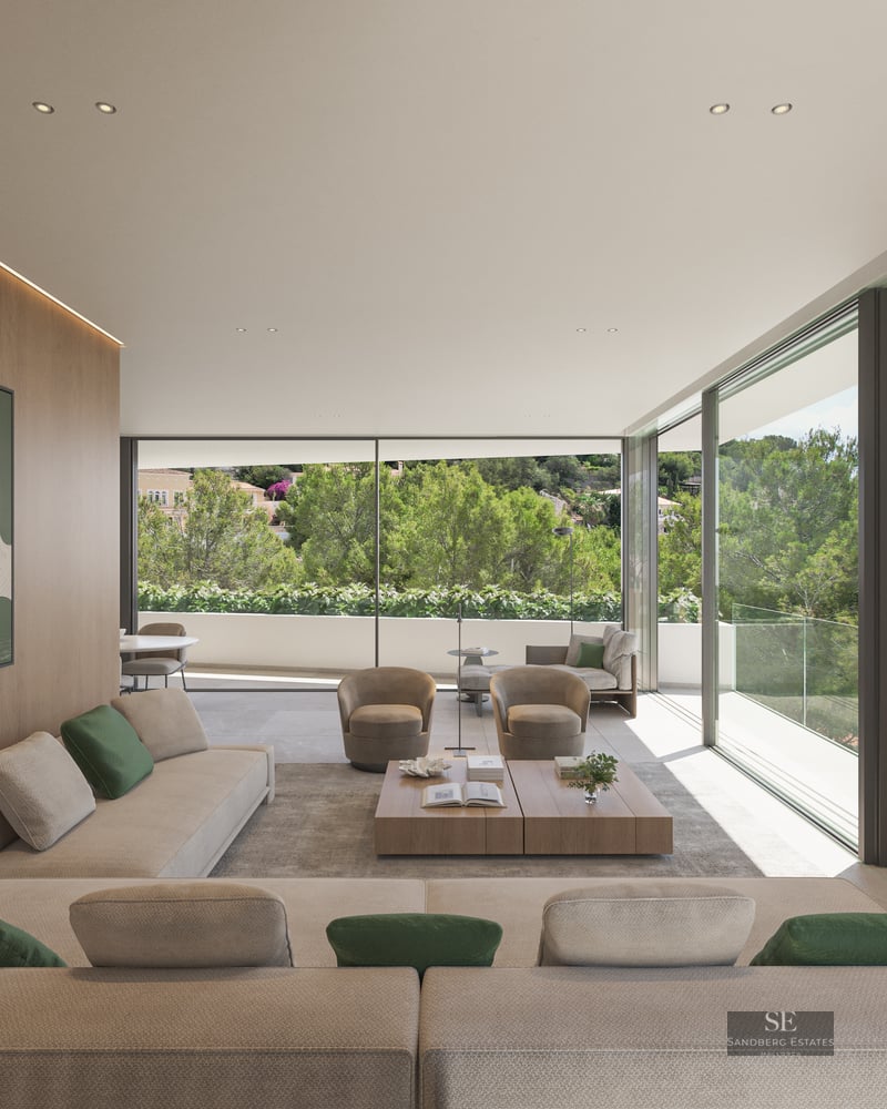 Spacious luxury living room featuring cream sofas, a wood-paneled wall, and floor-to-ceiling windows overlooking a lush forest.