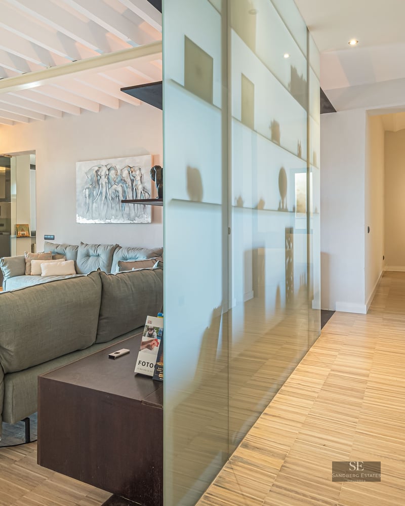 Living room featuring a grey sofa, wooden floors, a natural stone wall, and a frosted glass partition.