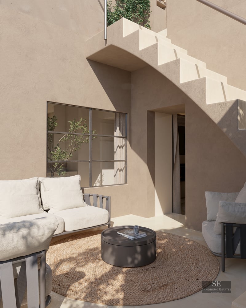 Sofa and armchair on a beige stucco terrace next to an exterior staircase and a round rug.