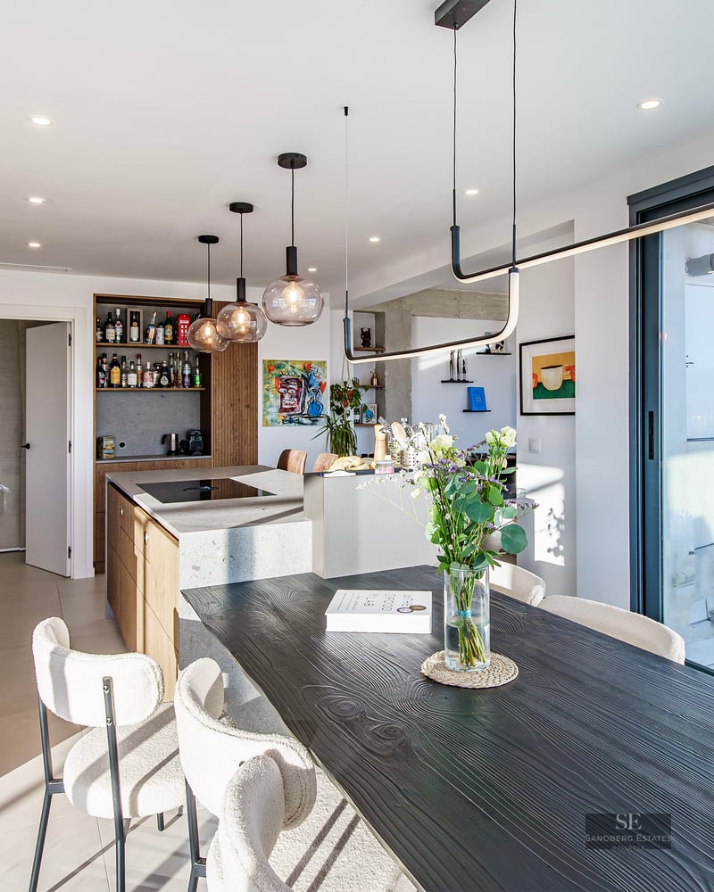 Modern kitchen with stone island and black wooden dining table with cream bouclé chairs.