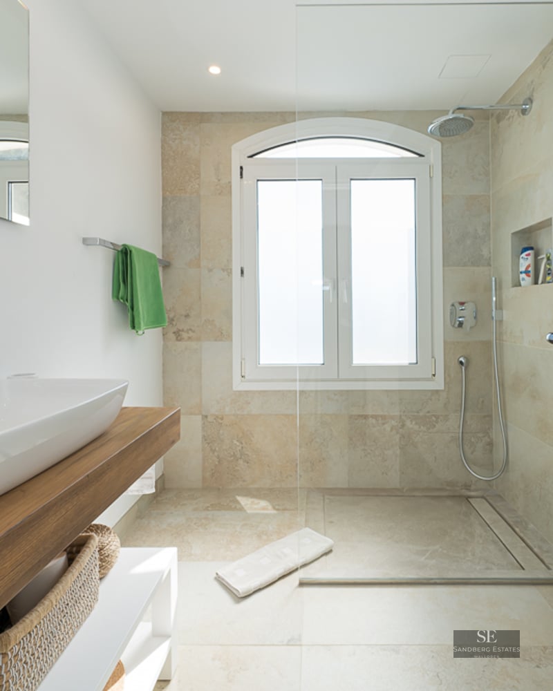 Salle de bain lumineuse avec vasque sur plan en bois et douche en pierre avec fenêtre cintrée.