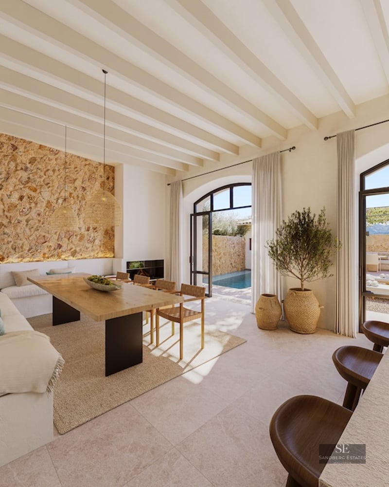 Elegant dining area featuring a natural stone wall, wooden beams, and large arched doors opening to a swimming pool.