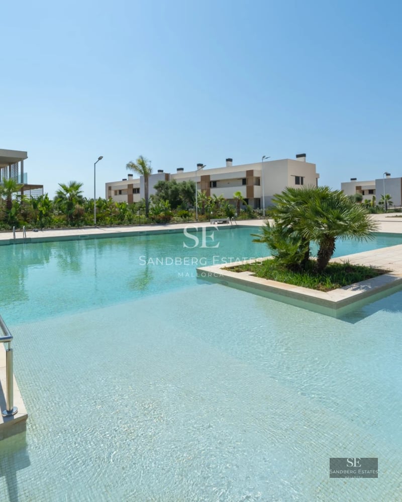 Wide view of a luxurious house featuring a turquoise pool and lush garden. Modern design, palm trees, and clear sky.