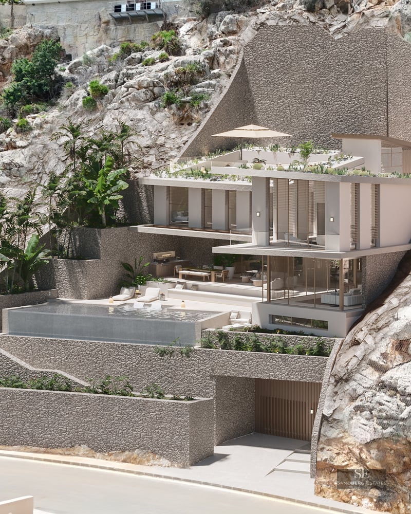 Modern multi-level villa built into a rocky cliff with an infinity pool, glass walls, and lush tropical greenery.
