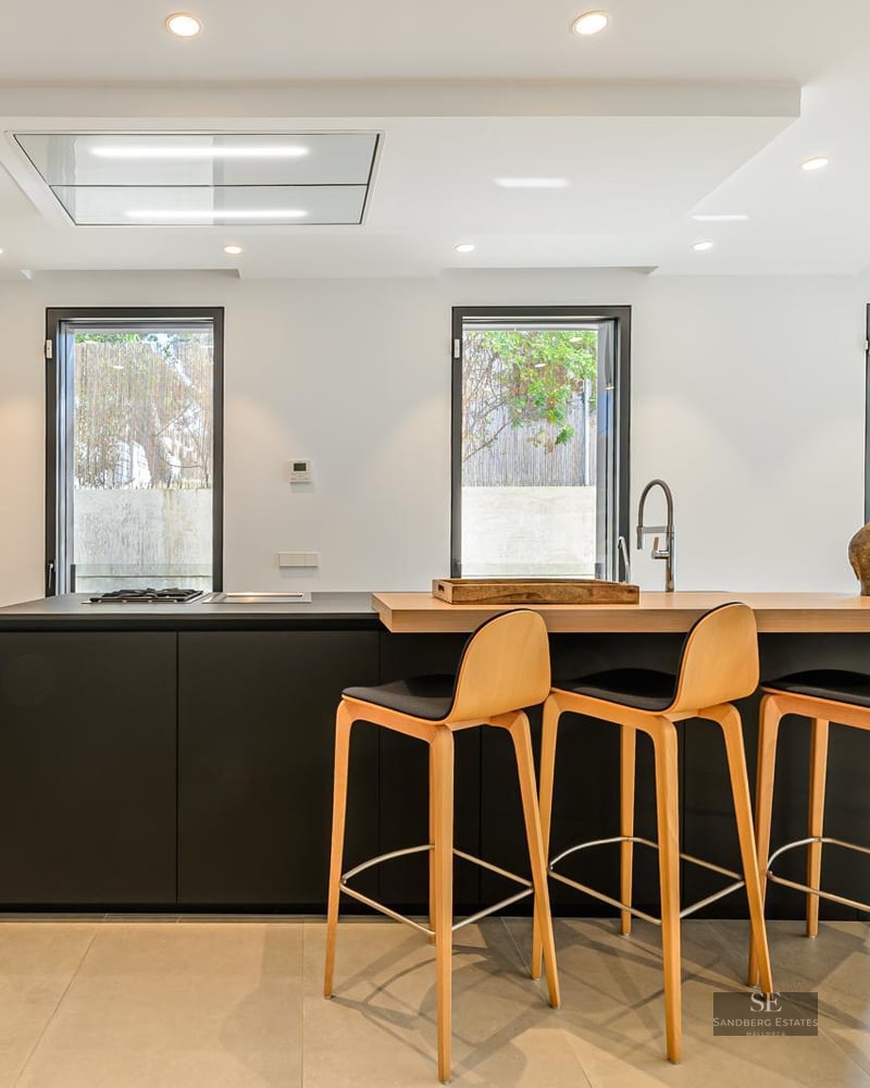 Modern kitchen featuring a black island with wooden breakfast bar, four stools, and floor-to-ceiling wooden cabinets.