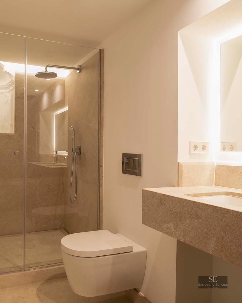 Modern bathroom featuring a glass-enclosed shower, a floating toilet, and a stone vanity with a backlit mirror.