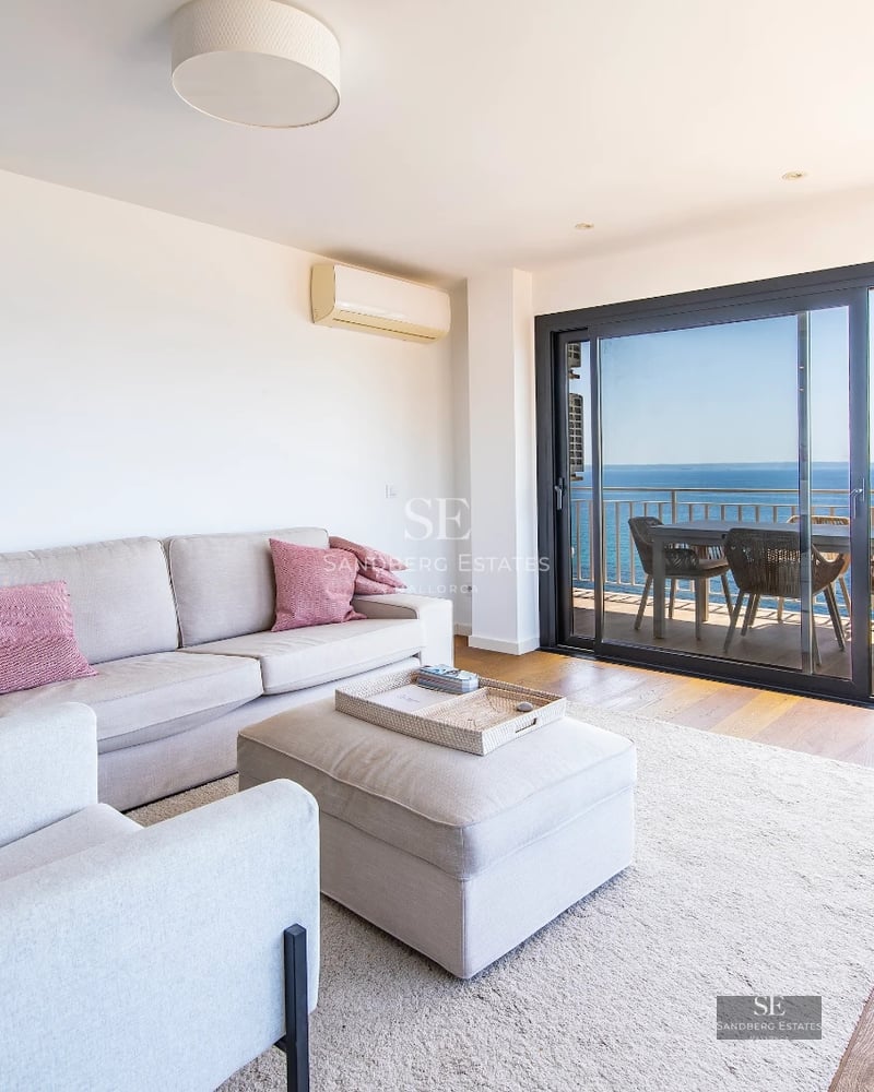Bright modern interior with sea views. Balcony with glass railing, stylish furniture, and a pool visible outside.