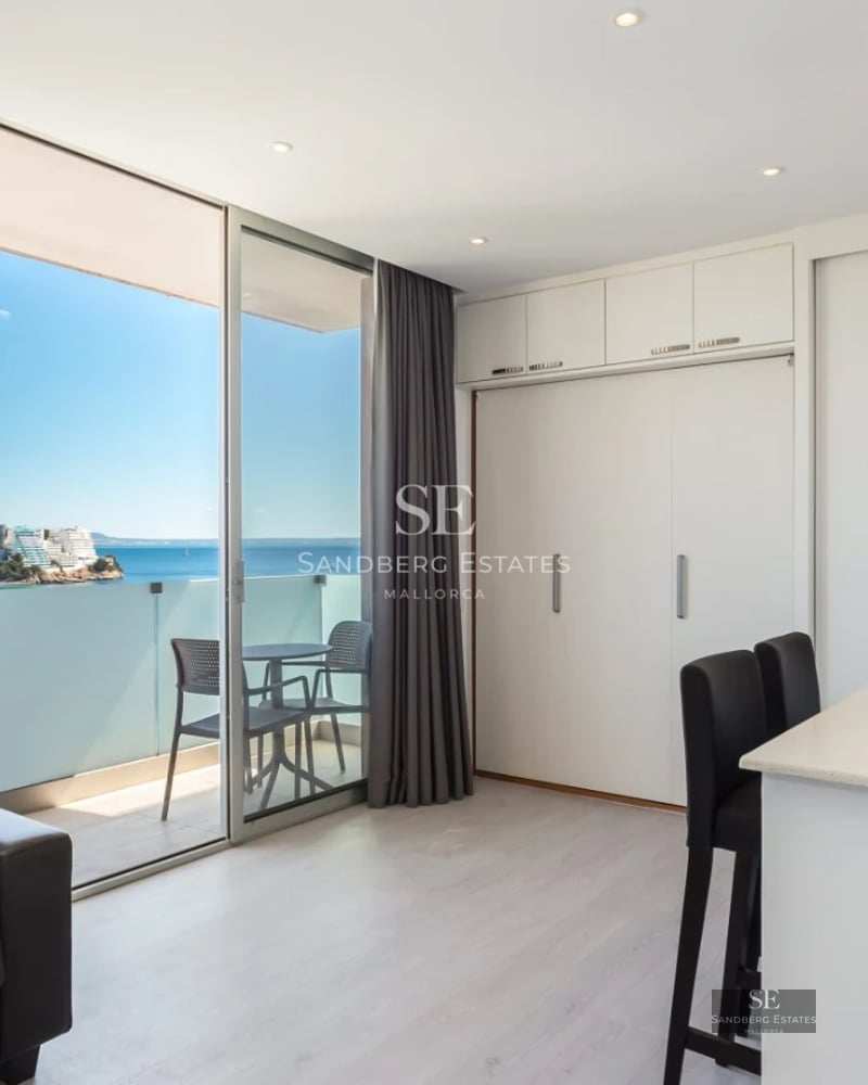 Spacious living room with large windows, light wood floors, and minimalist decor. Natural lighting highlights soft textures and neutral colors.