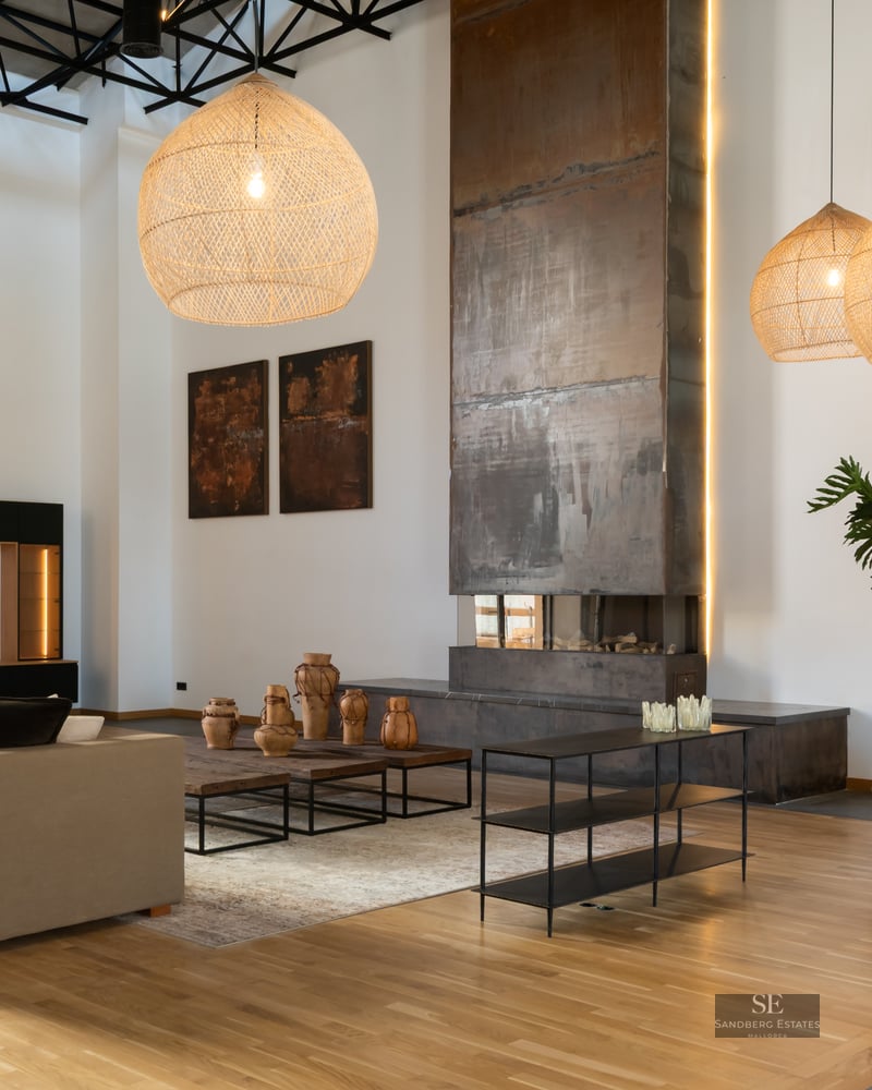 Spacious living room with high ceilings, large metal fireplace, wicker pendant lights, and modern beige sofa.