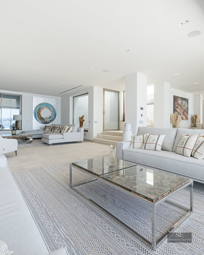 Spacious modern living room with grey sofas, glass coffee tables, and a view of the open-concept kitchen.