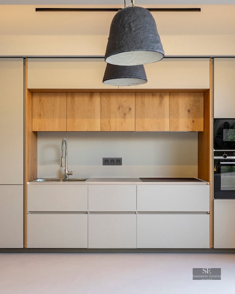 Cuisine moderne aux meubles crème, détails en chêne, appareils intégrés et grandes suspensions texturées.