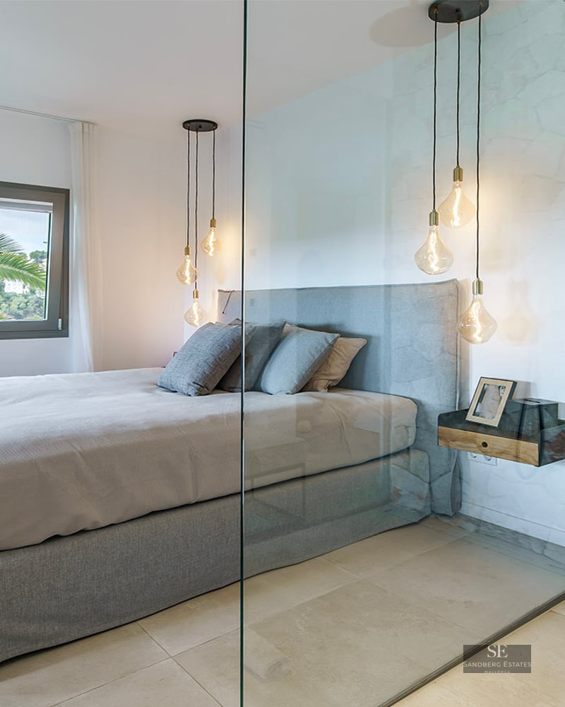 Contemporary bedroom with a grey bed, glass wall divider, and a rustic stone shower with brass fixtures.