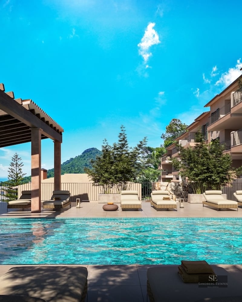 Turquoise swimming pool with sun loungers under a wooden pergola overlooking mountains and the sea under a blue sky.