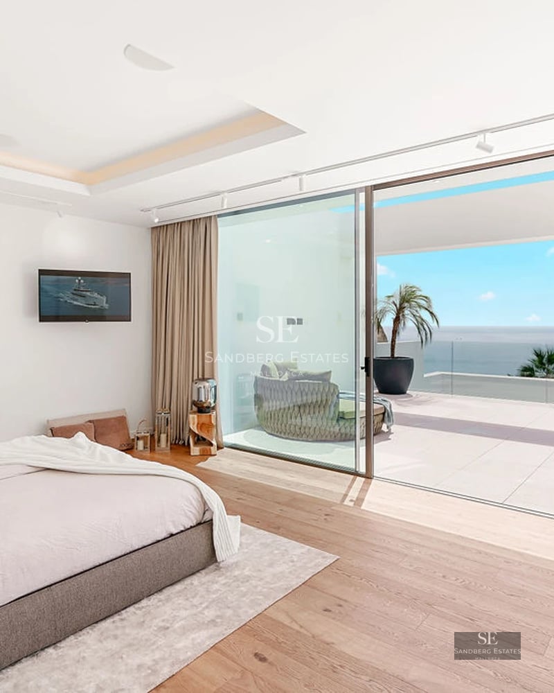 View of reflecting pool bordered by green grass. Lounge chairs, umbrellas, plants. Modern house in the background.