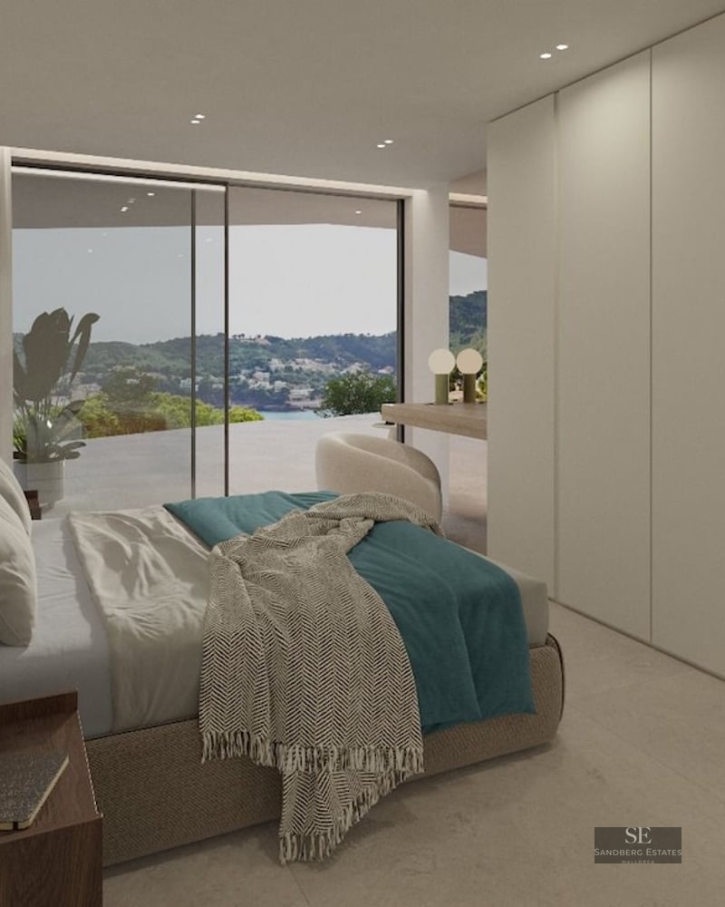 Minimalist bedroom with upholstered bed, built-in wardrobes, and glass doors opening to a scenic mountain and sea view.
