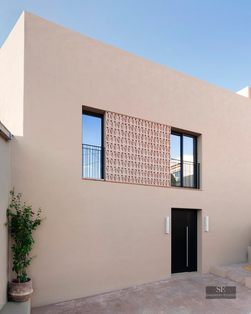 Façade beige avec porte noire, fenêtres à balustrades et écran décoratif en terre cuite.