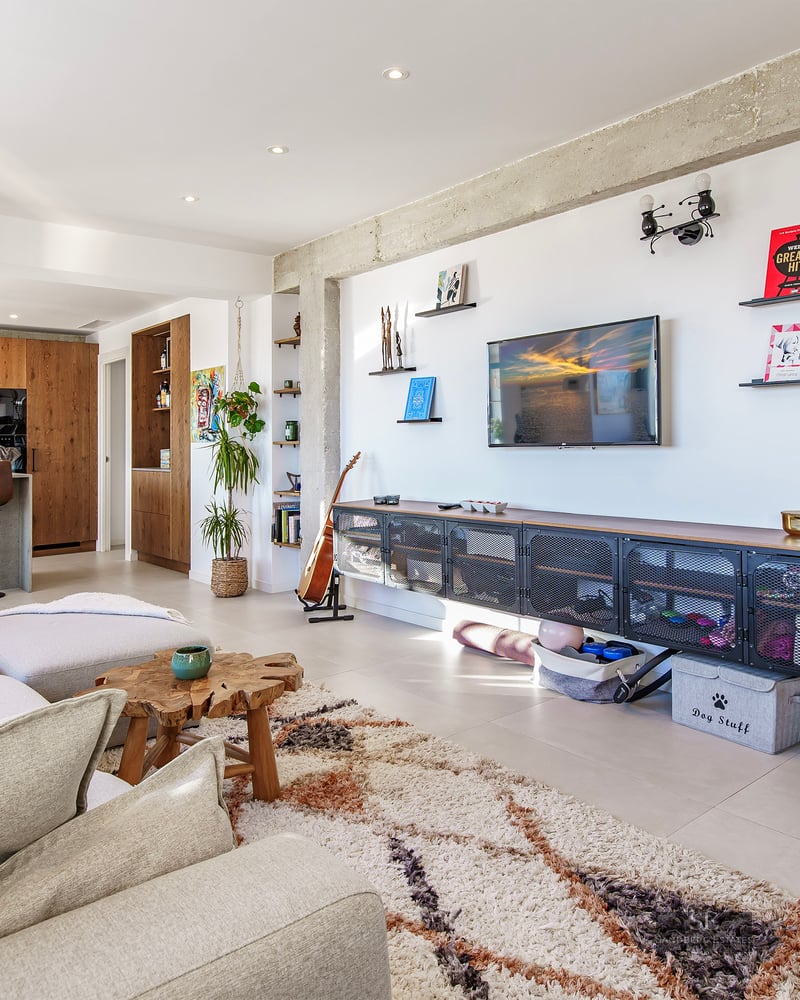 Spacious living room featuring a beige sectional sofa, shaggy rug, exposed concrete beams, and an open-plan kitchen.