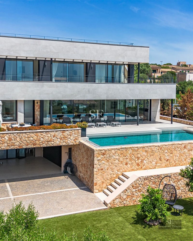 Spacious, bright living room with large windows, light wood floor, and modern furniture. Garden view with pool.