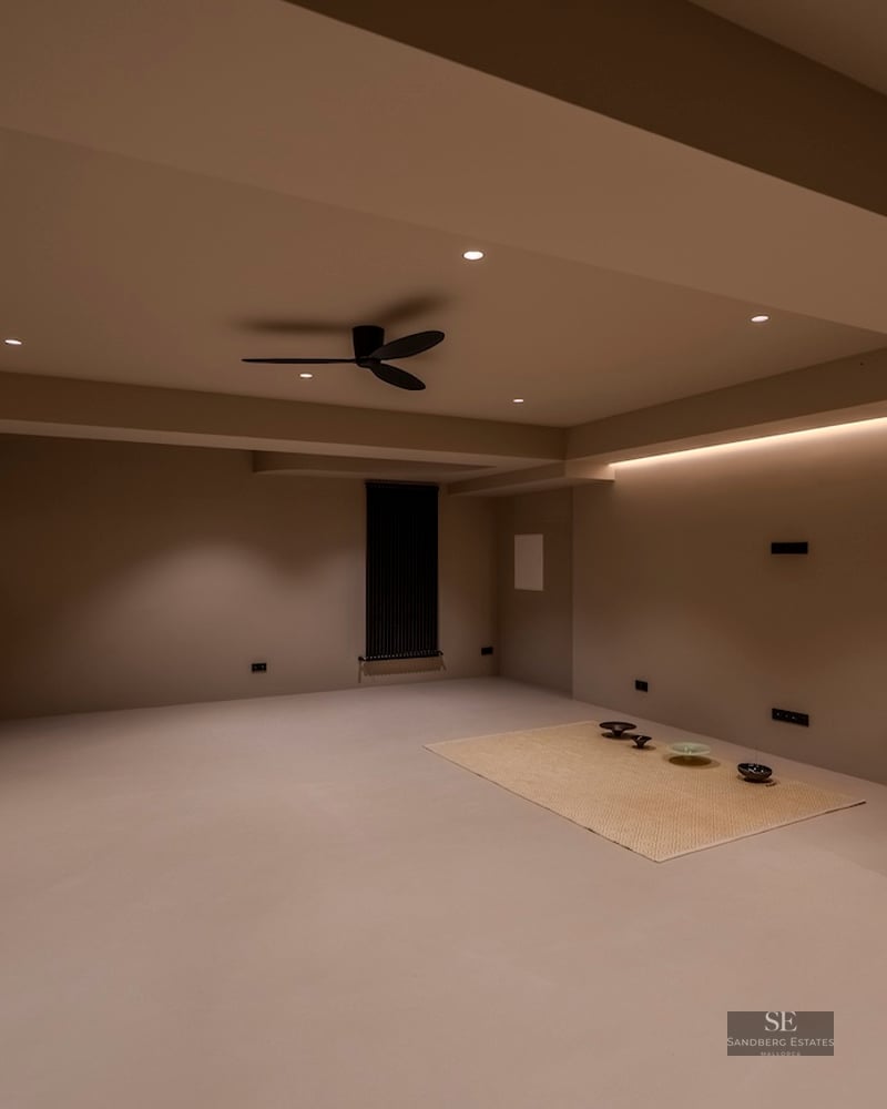 Pièce minimaliste vide avec murs beiges, éclairage LED indirect et ventilateur de plafond noir moderne.