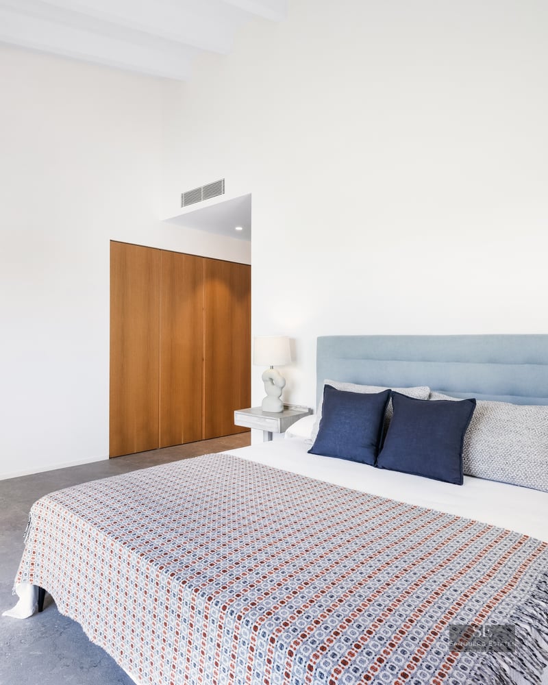 Bright bedroom with a large bed, light blue headboard, designer lamps, and built-in wooden wardrobe.