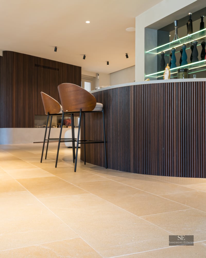 Modern living room featuring a curved wooden bar, designer stools, stone floors, and a bright red gorilla sculpture.