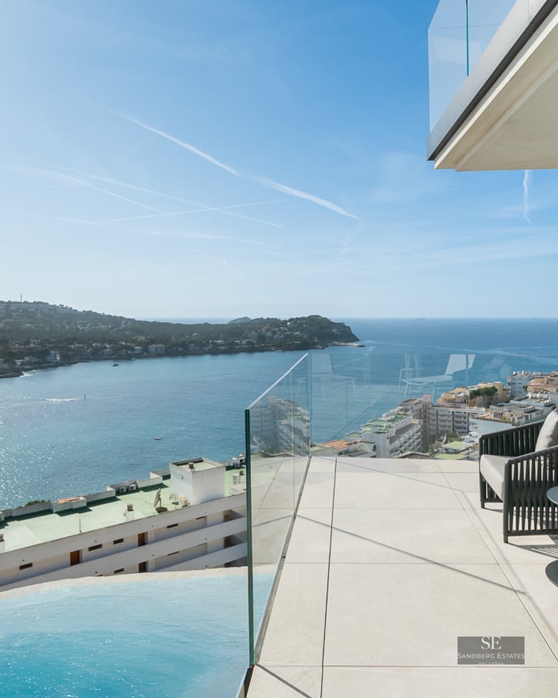 Modern terrace with designer chairs, glass railing, and views over a blue bay and infinity pool.