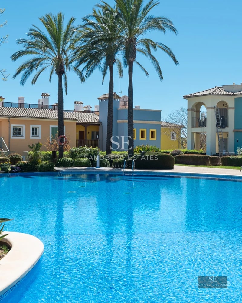 Image of a luxurious villa with infinity pool, manicured lawn, and modern architecture. Clear sky in the background.