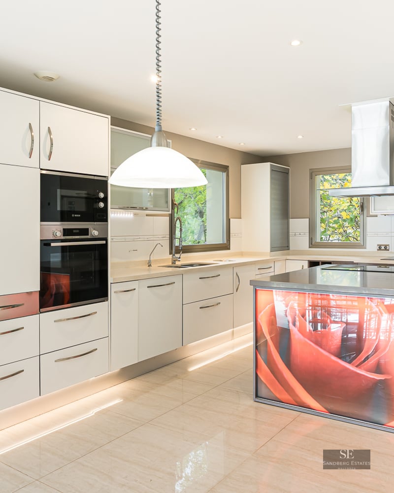 A bright, modern kitchen with white cabinets, stainless steel appliances, and a unique illuminated orange rose island.