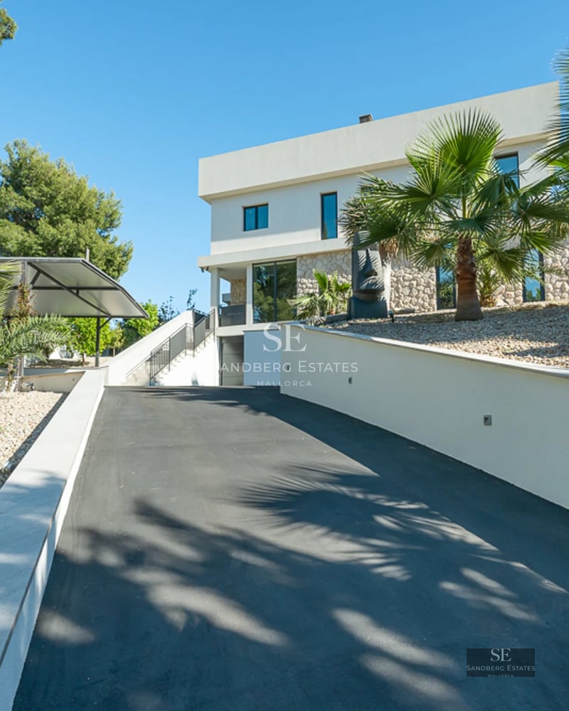 Large swimming pool with sun loungers, green garden, and modern facade of a detached house with large windows. Clear blue sky.
