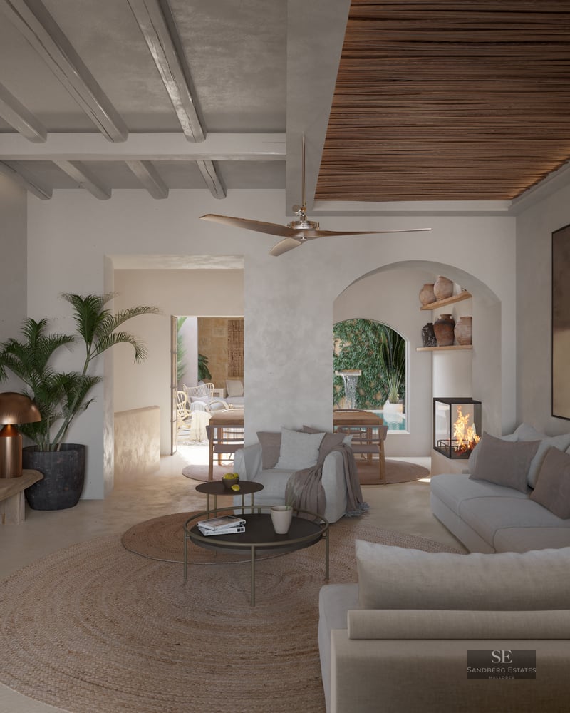 Luxurious living room featuring beige sofas, beamed ceilings, a modern fireplace, and views to a courtyard pool through an arch.