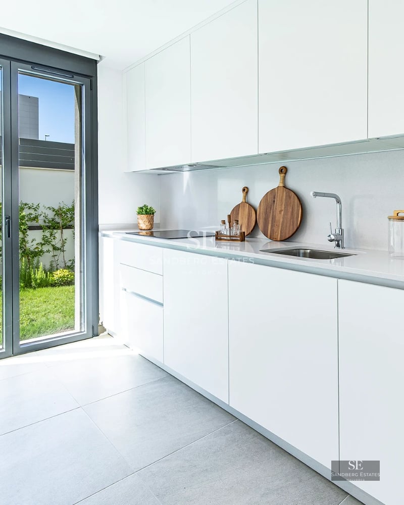 View of a luxurious pool with sun loungers and umbrellas, surrounded by greenery and a modern house with large windows.