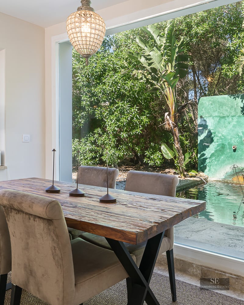 Contemporary dining room featuring a rustic wood table looking out onto a lush garden with a water pond.