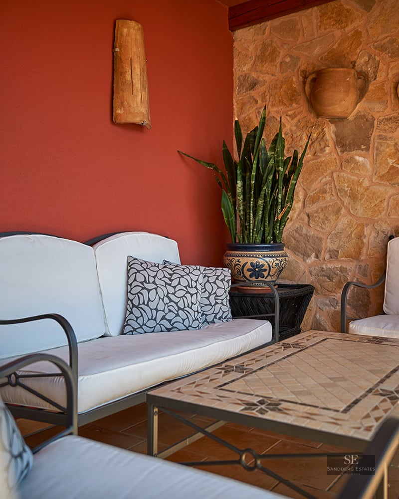 A terrace with white sofas, a mosaic table, a natural stone wall, and a vibrant red accent wall.