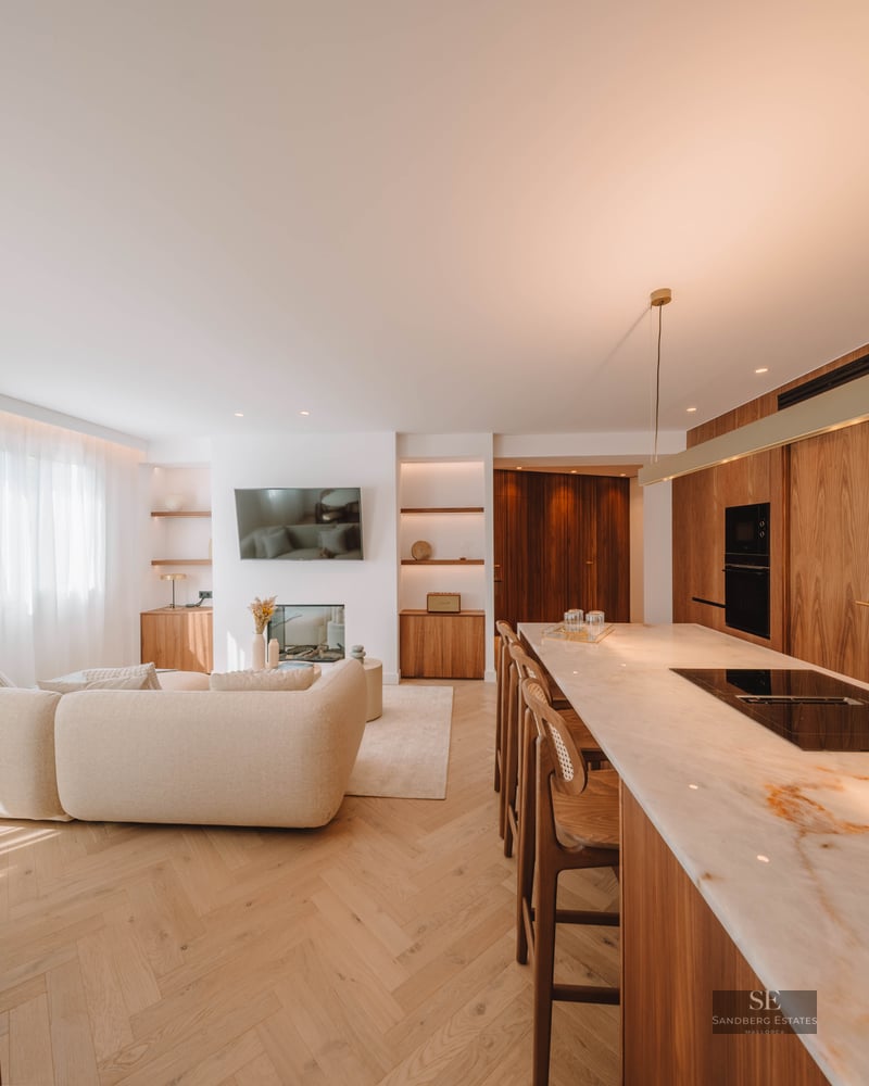 Bright open-concept living area with a beige sofa, marble kitchen island, and warm wood flooring.