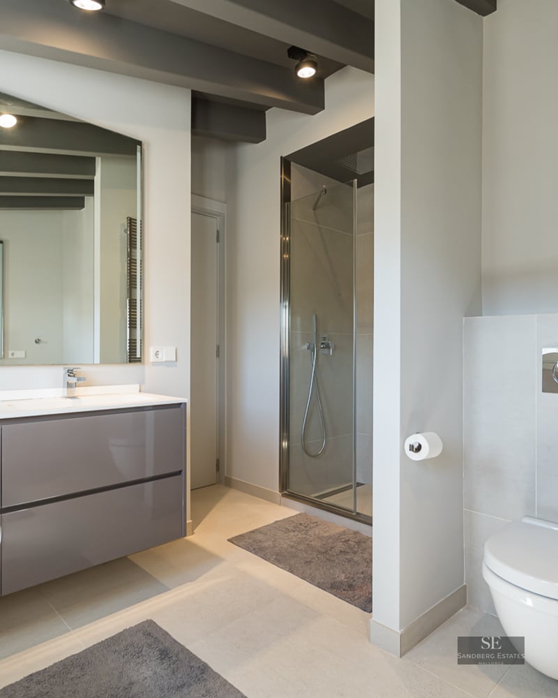 Modern bathroom featuring a grey floating vanity, glass walk-in shower, wall-mounted toilet, and exposed ceiling beams.
