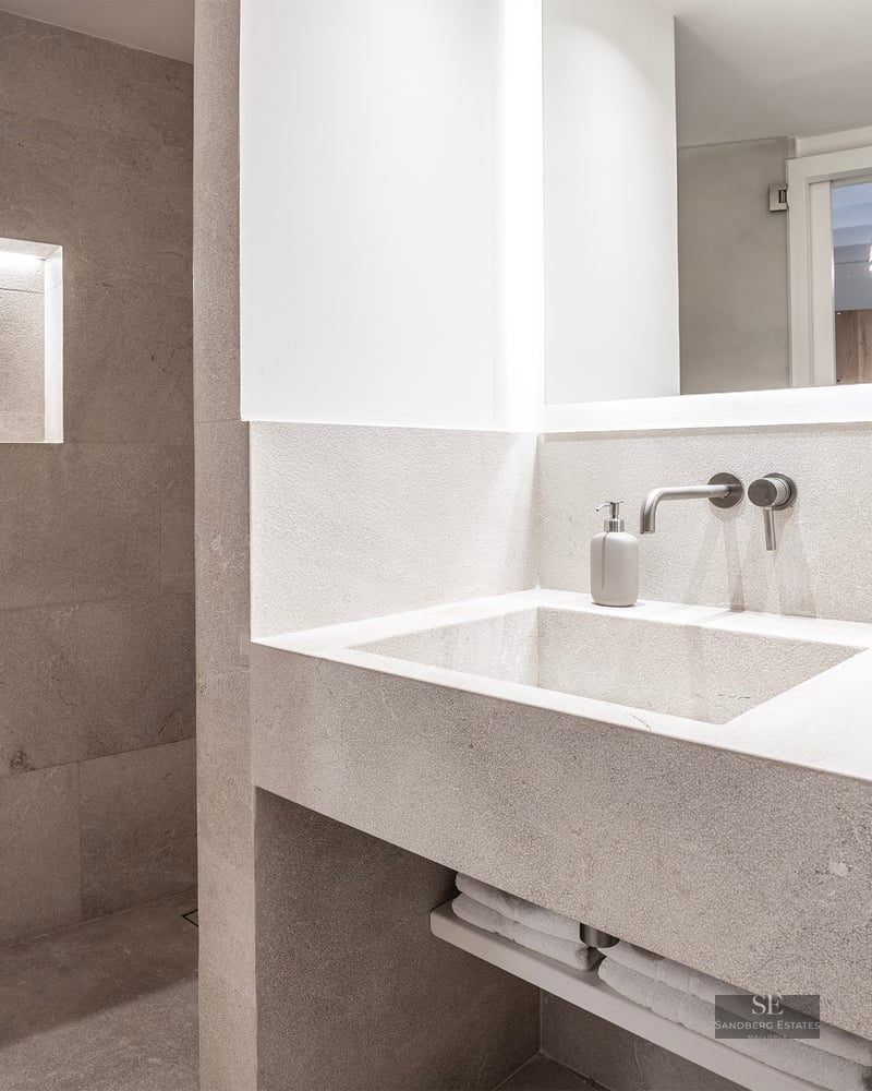 Modern bathroom featuring an integrated stone vanity, backlit mirror, and a walk-in shower with a lighted recessed niche.