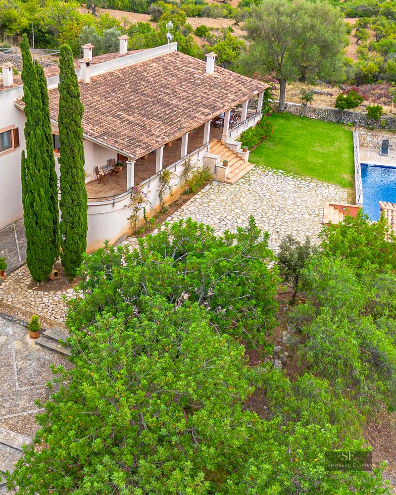 High-angle view of a villa with a terracotta roof, stone courtyard, blue swimming pool, and lush green landscaping.
