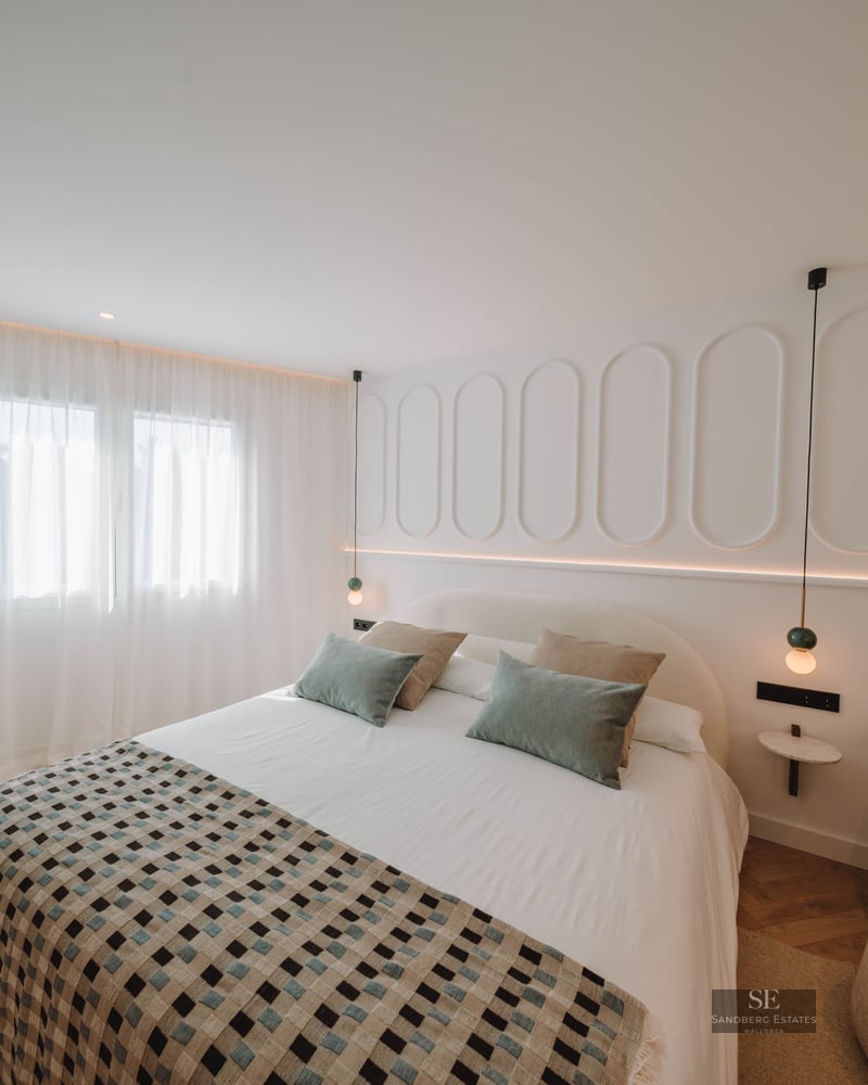 Bright bedroom featuring a large bed, white walls with oval molding, and elegant herringbone wood flooring.