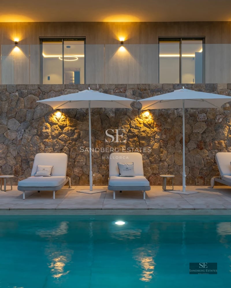 View of a luxurious pool surrounded by manicured garden. Modern design, stylish sun loungers and lush green vegetation.