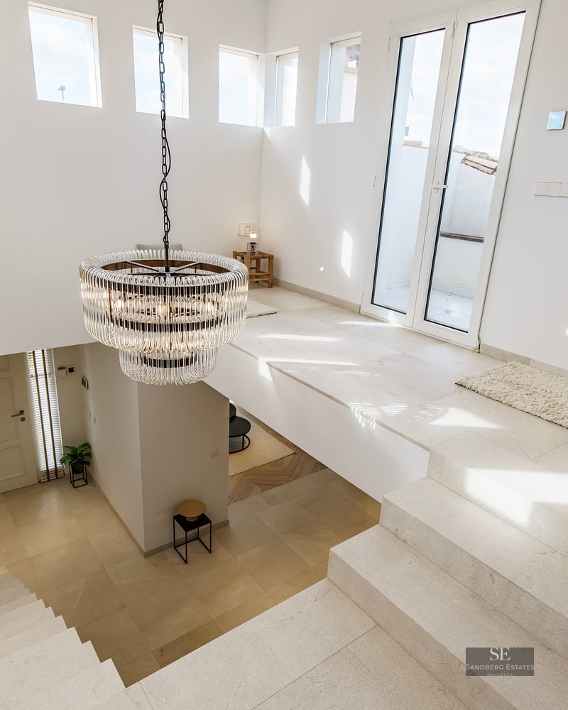 High-angle view of a bright modern foyer with stone stairs, white walls, and a large crystal chandelier.